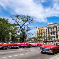 鮮やかな赤色のレトロカーが並ぶキューバ風の街角の写真