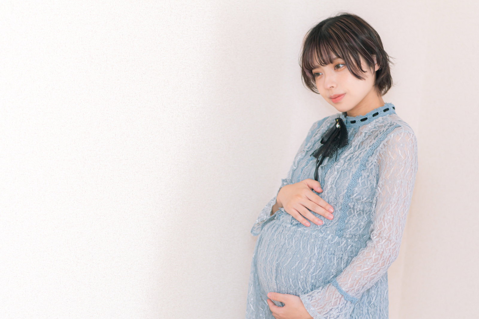 水色のシャツを着て臨月のお腹に手を当てて立つ妊婦［モデル：高尾実生］