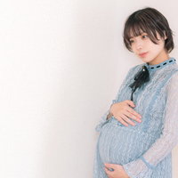 臨月の妊婦が両手でお腹を支える水色シャツの女性の写真