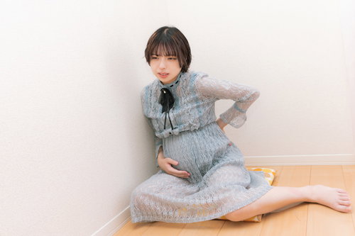 グレーのパジャマを着た妊娠後期の腰痛に悩む妊婦