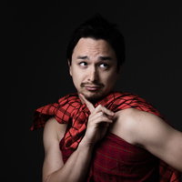 赤いチェック柄のマサイ族衣装を着て考え事をするドイツ人ハーフ男性の写真