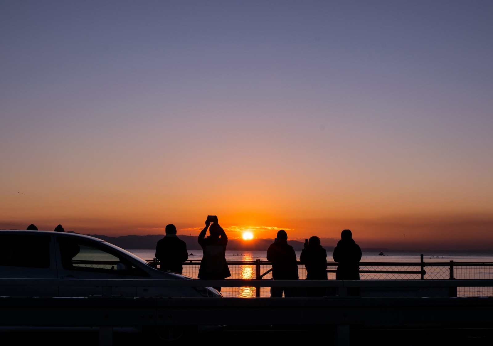 海岸で初日の出を撮影する人々のシルエット、オレンジ色の夕焼け空