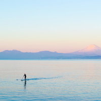 富士山をバックに夕焼けの海でスタンドアップパドルボードを楽しむ男性の写真