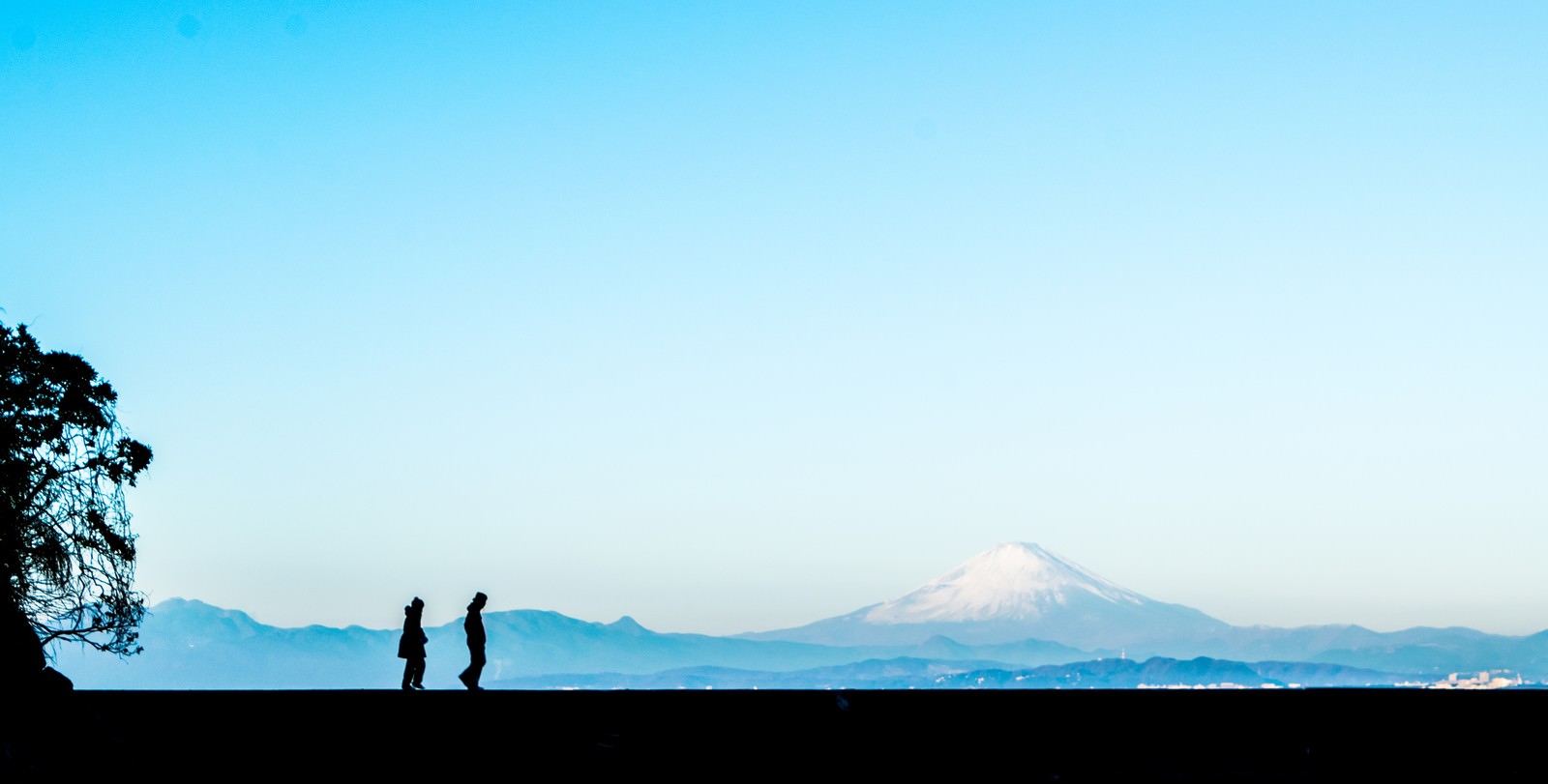 富士山を背景に散歩するカップルのシルエットが青空に映える風景