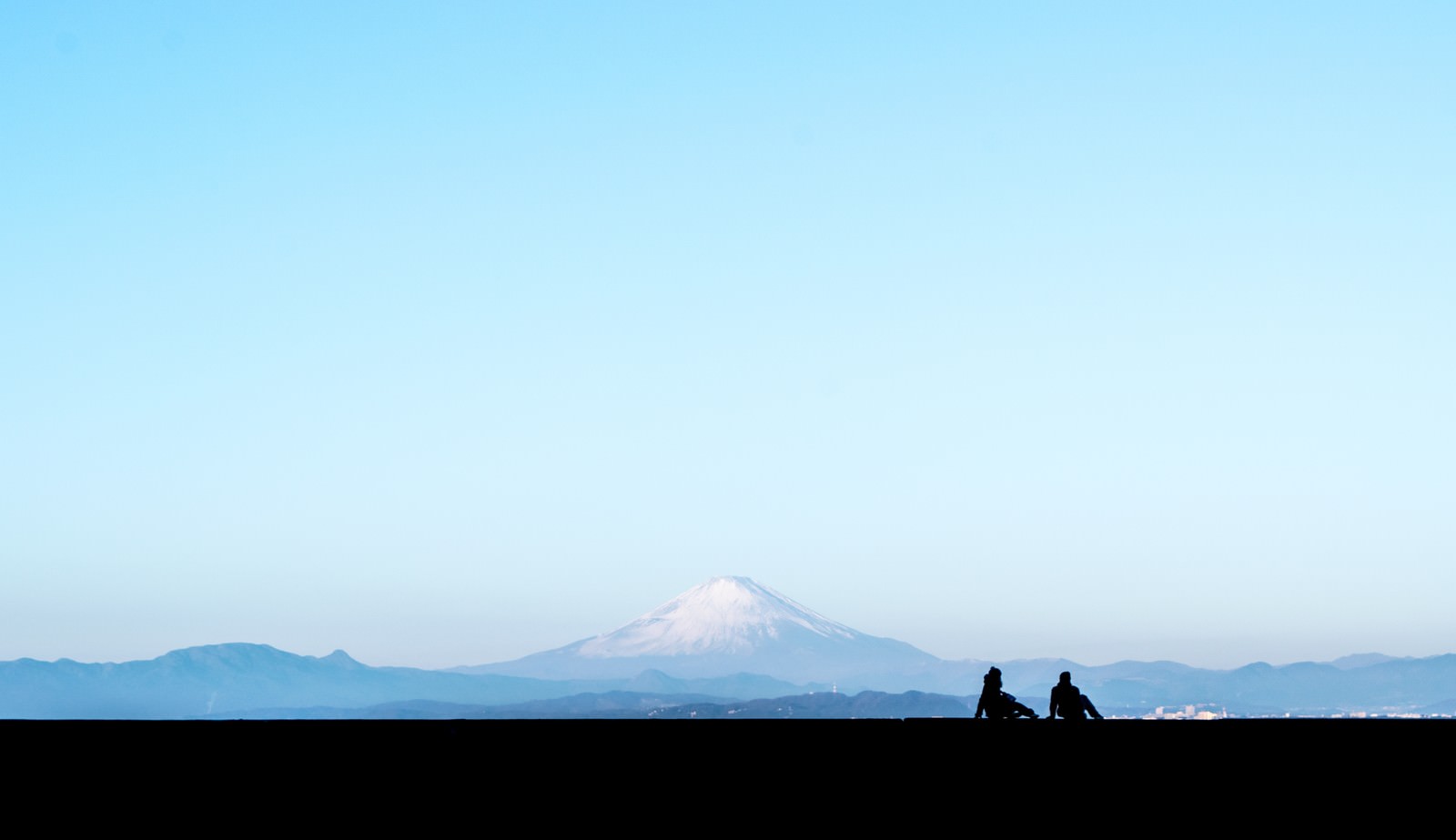 青空と富士山を背景に座るカップルのシルエット