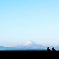 富士山を見つめるカップルのシルエット、青空の下で座る恋人たちの写真