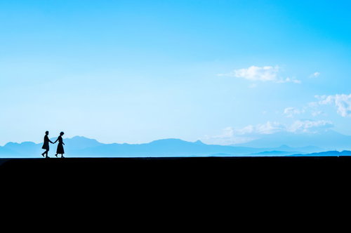 うつむき歩く彼女と手を繋ぐ彼氏のシルエット