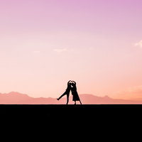 夕焼け空を背景に寄り添ってハートを作る男女のシルエットの写真