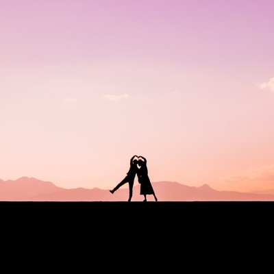 夕焼け空を背景に寄り添ってハートを作る男女のシルエットの写真