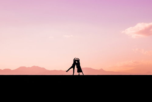 夕焼け空を背景に寄り添ってハートを作る男女のシルエット