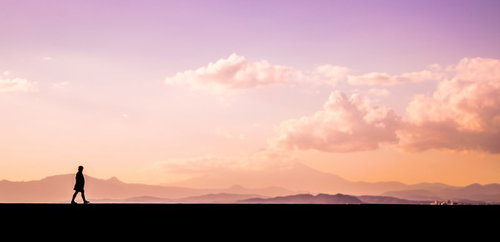 夕焼けの中を散歩する男性のシルエット写真