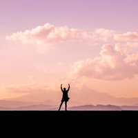 夕焼けに向かい両手をあげて何か叫ぶ女性のシルエットの写真