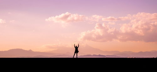 夕焼けに向かい両手をあげて何か叫ぶ女性のシルエット