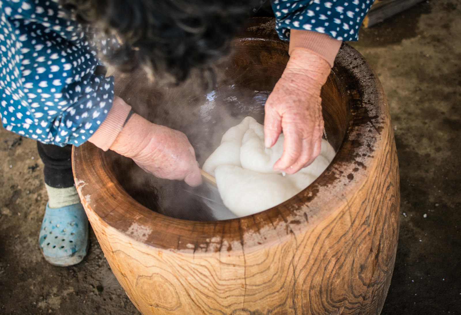 木製の臼の中でつきたての白い餅をひっくり返している手