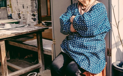 青い花柄の着物を着て椅子に腰掛け腕組みしながらひと休みする婆ちゃん