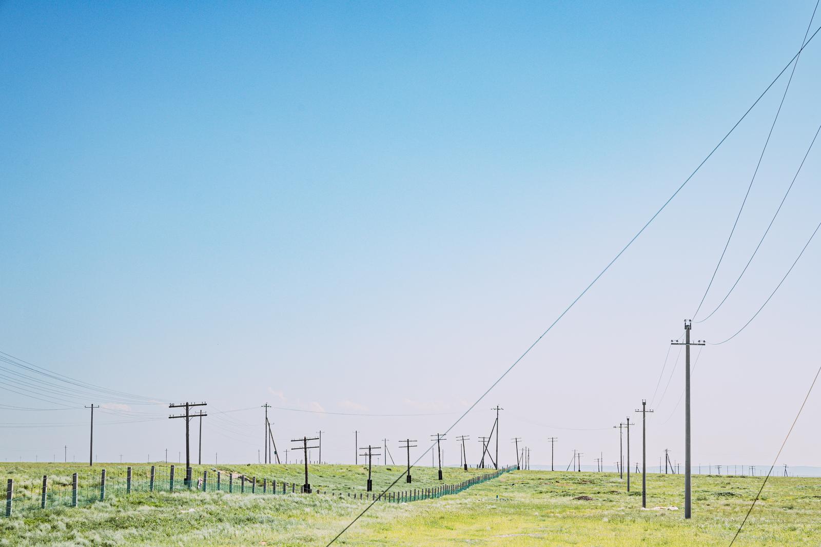 緑の草原に立ち並ぶ複数の電柱と送電線、晴れた青空