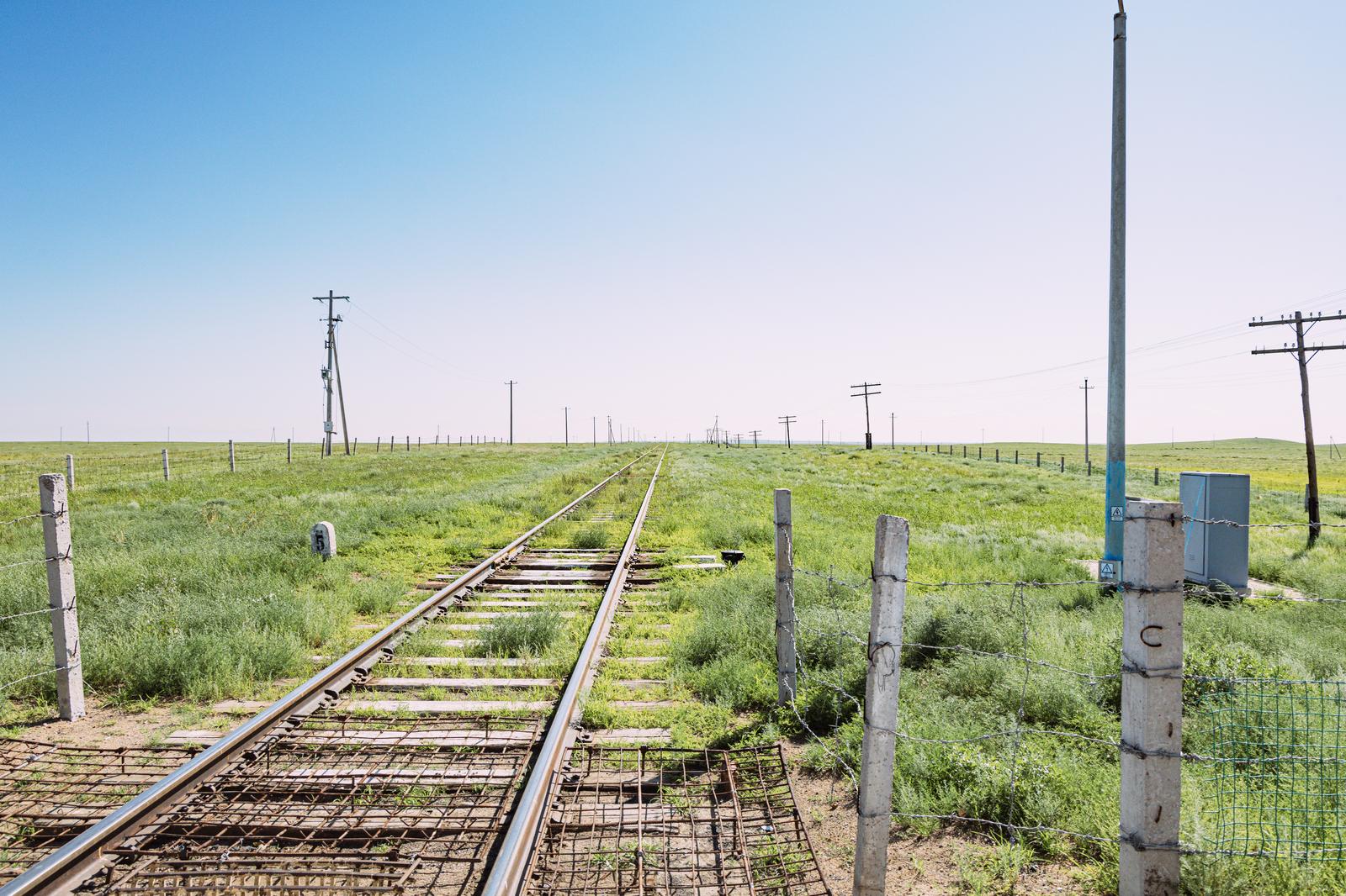 草原の中を地平線へ向かって伸びる廃線と電柱が立ち並ぶ風景