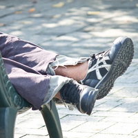 公園のベンチで横になる人の足元とスニーカーの写真