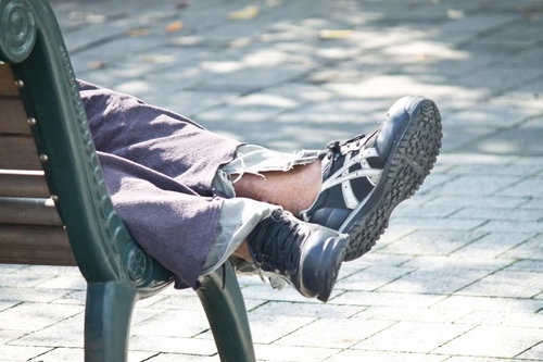公園のベンチで横になる人の足元とスニーカー