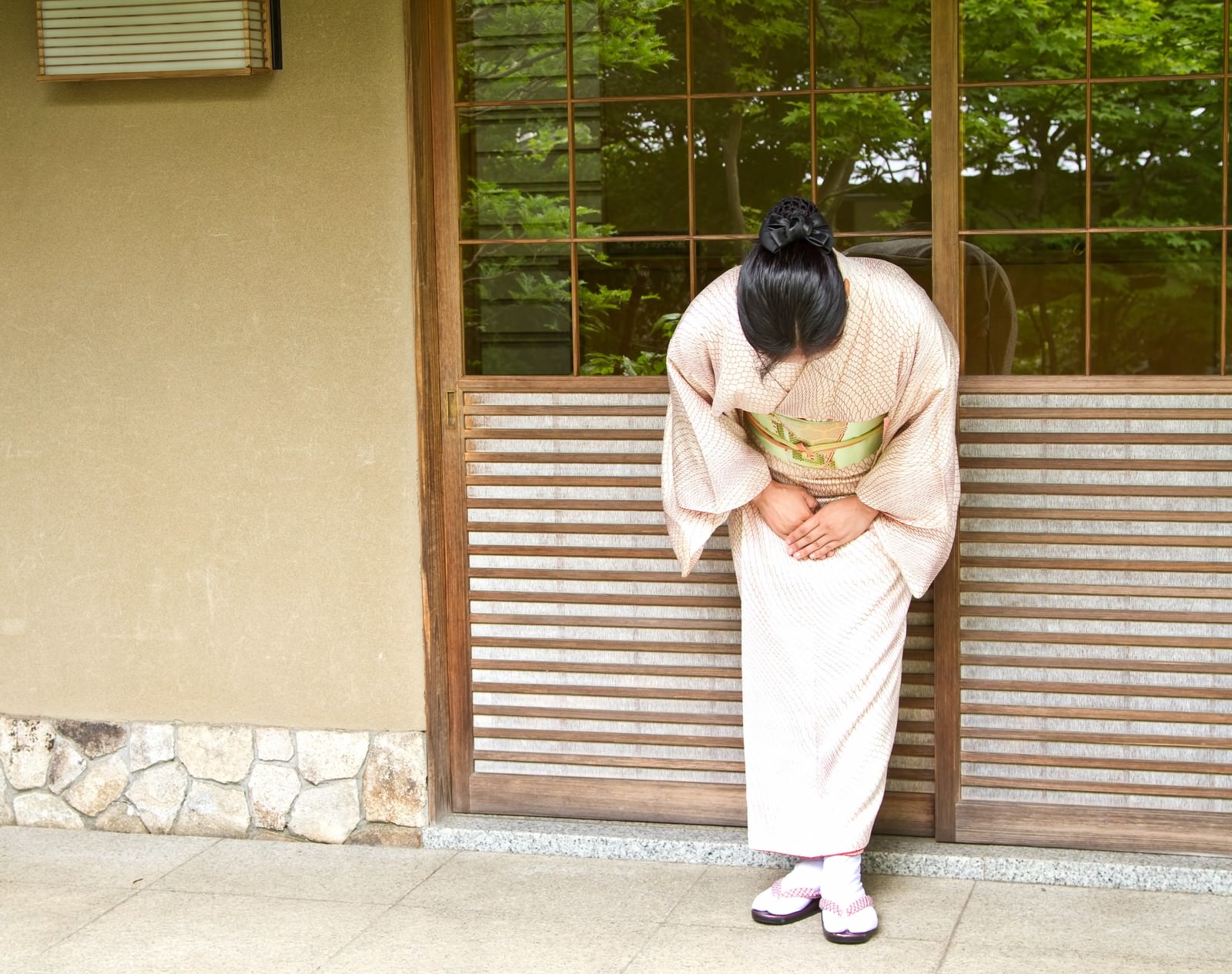玄関でお辞儀する女将さんの後ろ姿［モデル：きせんひろみ］