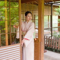 和風の暖簾がかかる玄関先に立つ着物姿の女将さんの写真