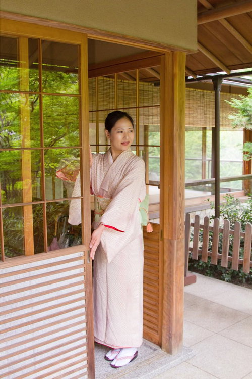 和風の暖簾がかかる玄関先に立つ着物姿の女将さん