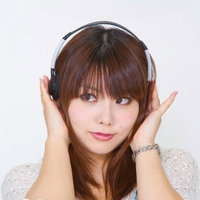 ヘッドフォンを両手で耳に当てて音楽を聴く女性の写真