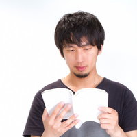 ソファーに座って開いた本を読む男性の横姿の写真