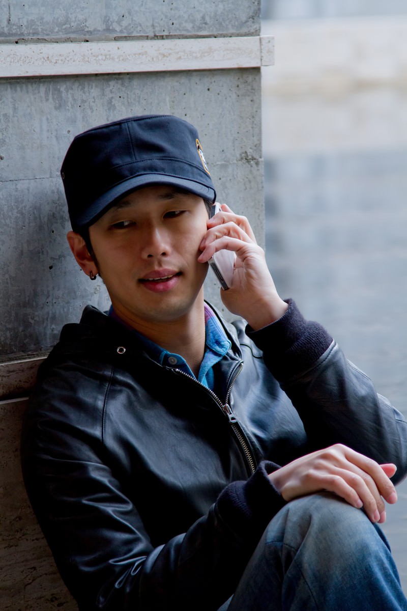 壁にもたれて電話をかける男性［モデル：大川竜弥］