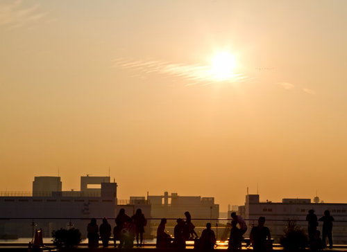 オレンジの夕焼け空を背景に歩く人々のシルエット