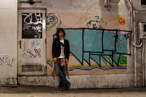 グラフィティの壁の前に立つジャケットの若者