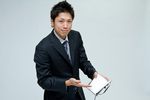 水色の壁の前でスケジュール帳を開いて見せるサラリーマン