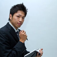 水色の壁の前でペンとメモ帳を持つスーツ姿のビジネスマンの写真