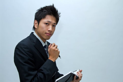 水色の壁の前でペンとメモ帳を持つスーツ姿のビジネスマン