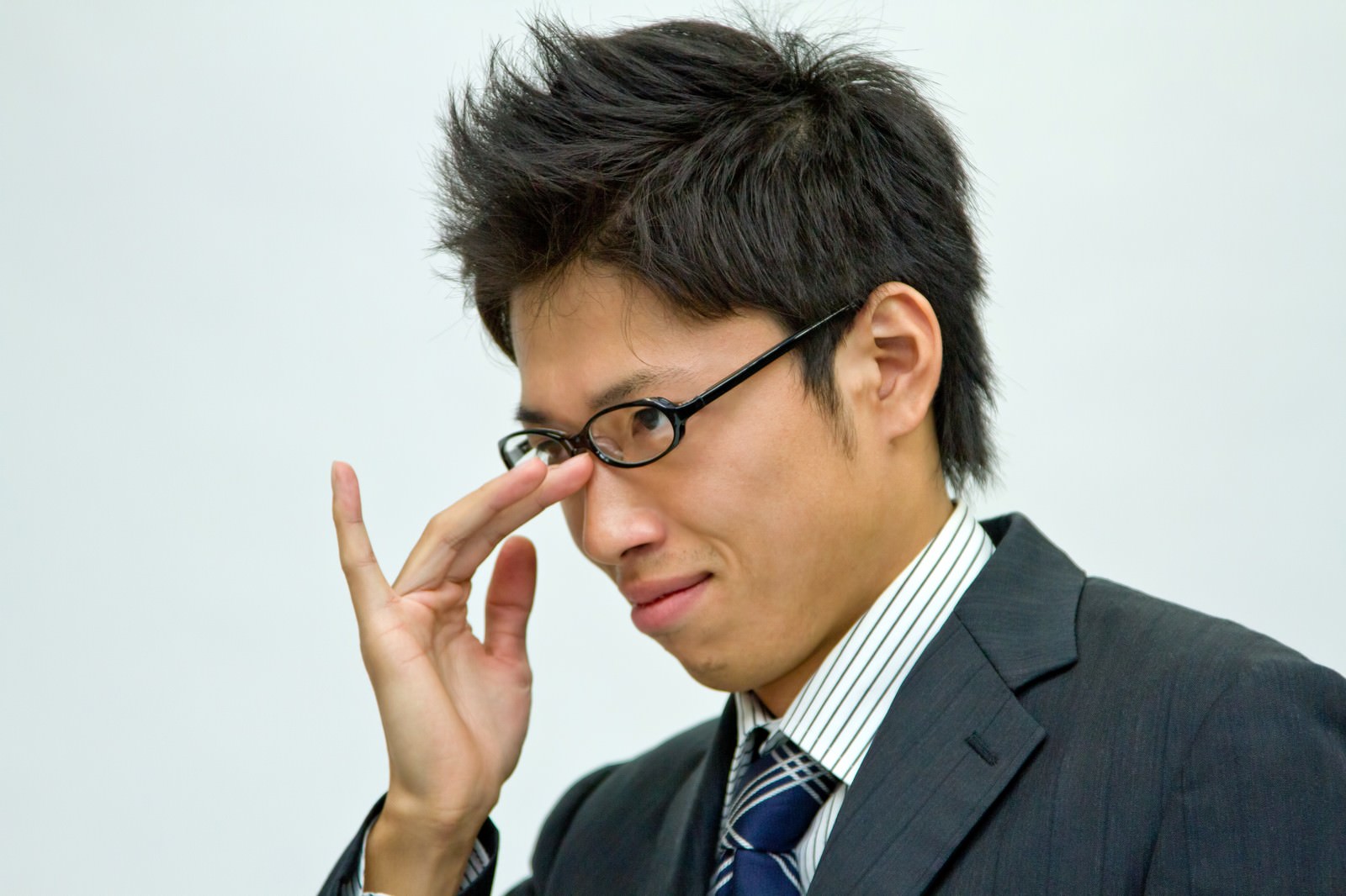 眼鏡に手を当てる悪巧み顔のビジネスマン［モデル：恭平］