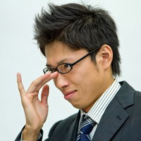 ダークスーツで眼鏡に手を当て悪巧みを考える横顔のビジネスマンの写真