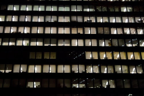 夜のオフィスビルの窓から漏れる明かりが並ぶ眠らないオフィス