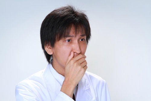 白衣を着て口元を手で覆い驚いた表情の男性