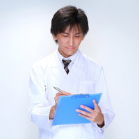 クリップボードにペンでメモを取る白衣の男性医師の写真