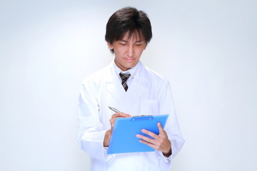 クリップボードにペンでメモを取る白衣の男性医師