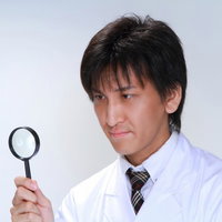 白衣を着て虫眼鏡を持ち何かを確認する男性の写真