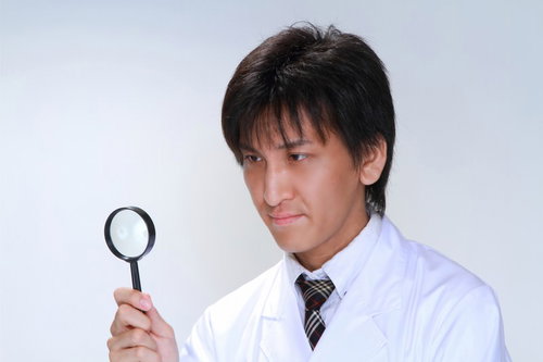 白衣を着て虫眼鏡を持ち何かを確認する男性