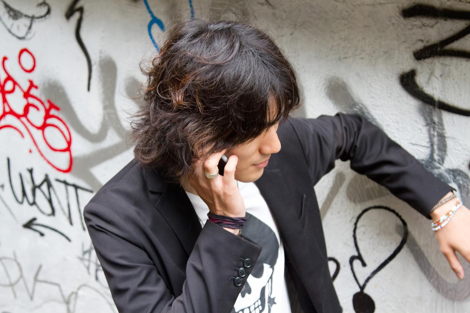 落書きの壁に手をかけ電話する男性［モデル：村田裕章］