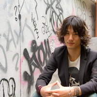 落書きだらけのかべの前でこちらを見る男性の写真