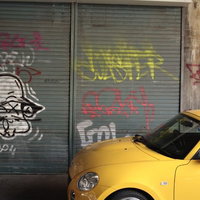 黄色い車が停まるシャッターに落書きされた壁の写真