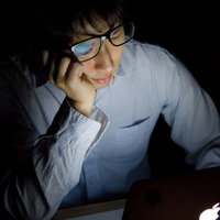 台風で帰宅できずに残業しうなだれる男性の写真