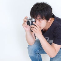 低い姿勢でしゃがんで一眼レフカメラを構える男性の写真