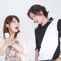 後ろから恋人の携帯電話の画面をこっそり覗き見する男性の写真