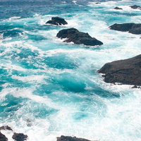 岩に波が打ち付けてしぶきが上がる石廊崎の海の写真