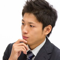 水色の壁の前で腕を組んで横目で様子をうかがうサラリーマンの写真